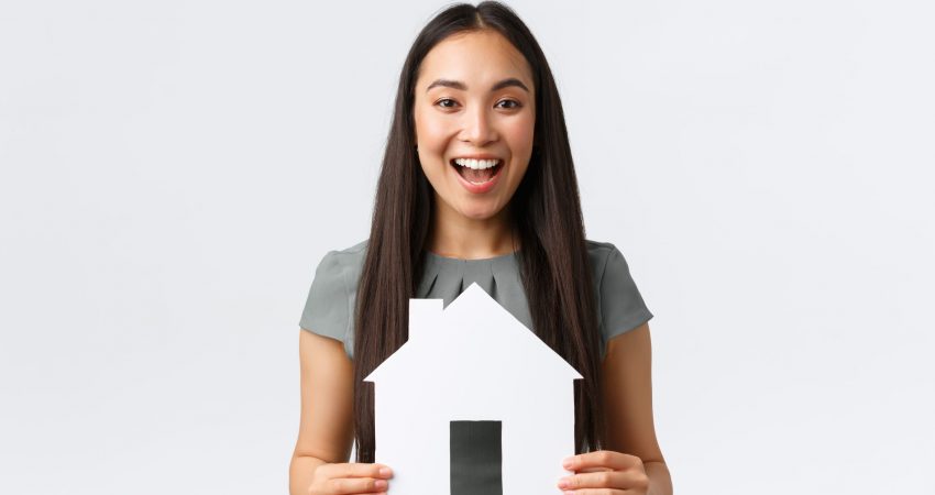 Insurance, loan, real estate and family concept. Cheerful asian female buying or selling home, holding paper house and smiling upbeat, searching for new apartment, white background.
